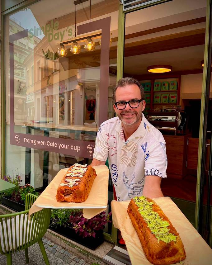 Der Inhaber vor dem Schaufenster mit dem Claim-Schriftzug, in jeder Hand ein frisch gebackenes Bananenbrot